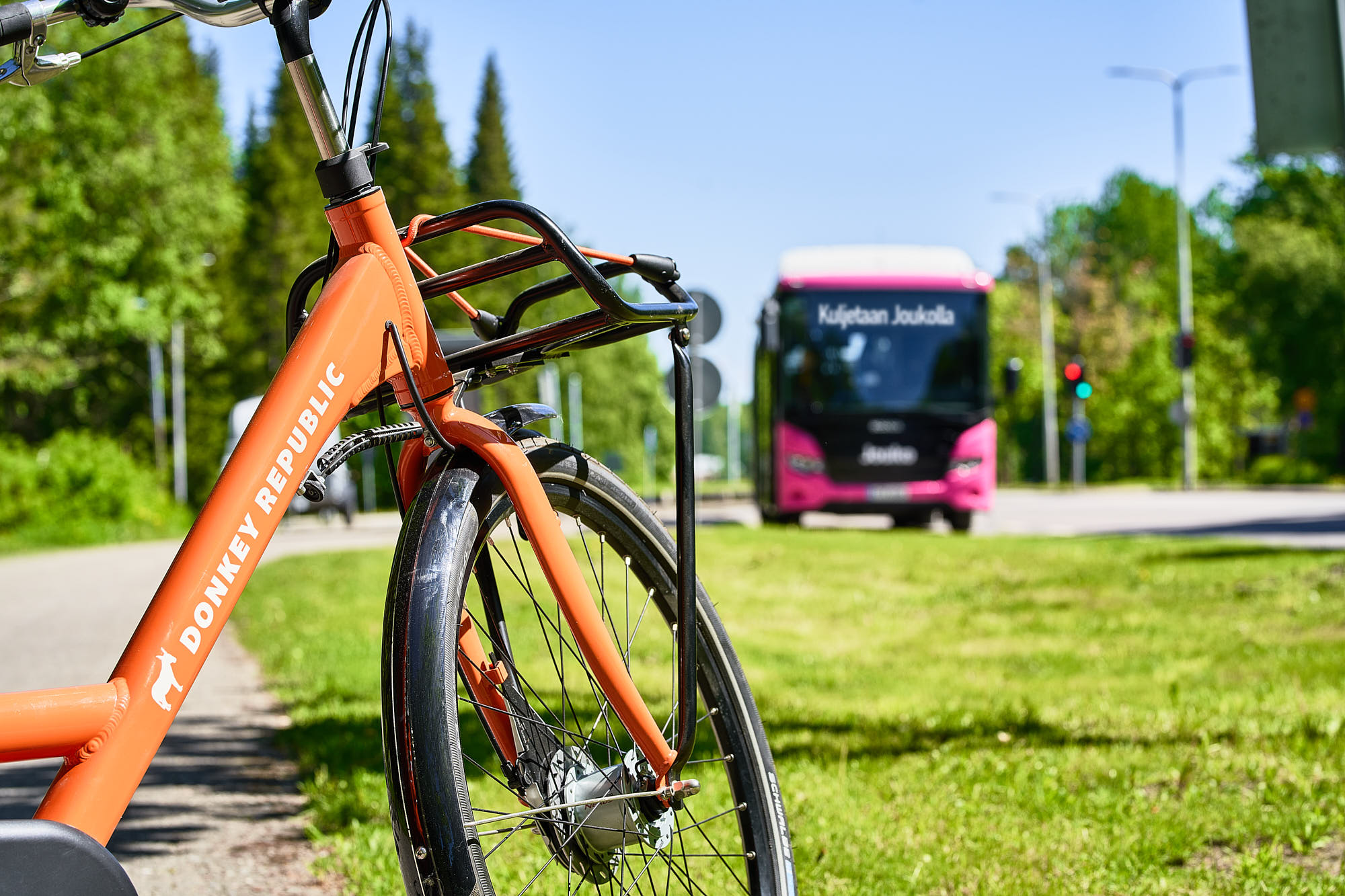 City bike and a pink bus. In the background, green grass and trees.